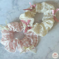 Two lace scrunchies with ribbons and pearls on a marble surface