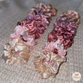 Set of four satin scrunchies in pink, purple, and gold on a textured surface.