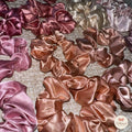 Collection of satin scrunchies in various pink and rose gold colors on a textured surface.