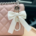 White bow keychain with pearl details on a pink quilted handbag.