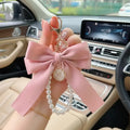 Pink bow keychain with pearl details held in front of a car interior.