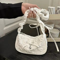 White handbag with a floral white texture and bow held by a person indoors.