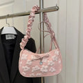 Pink lace handbag with floral patterns hanging on a rack next to a black jacket.