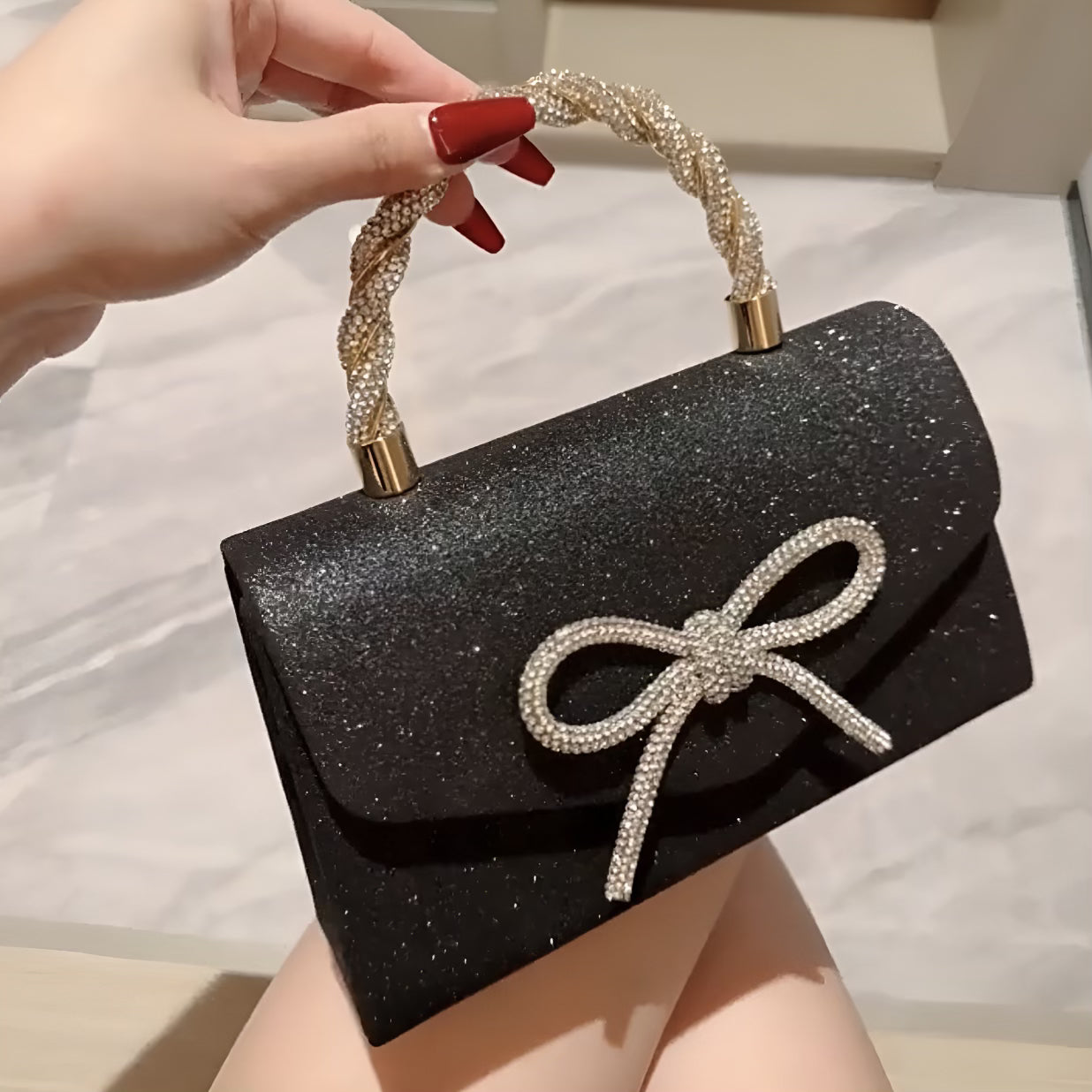 Black glittery handbag with a bow and gold accents held by a hand.