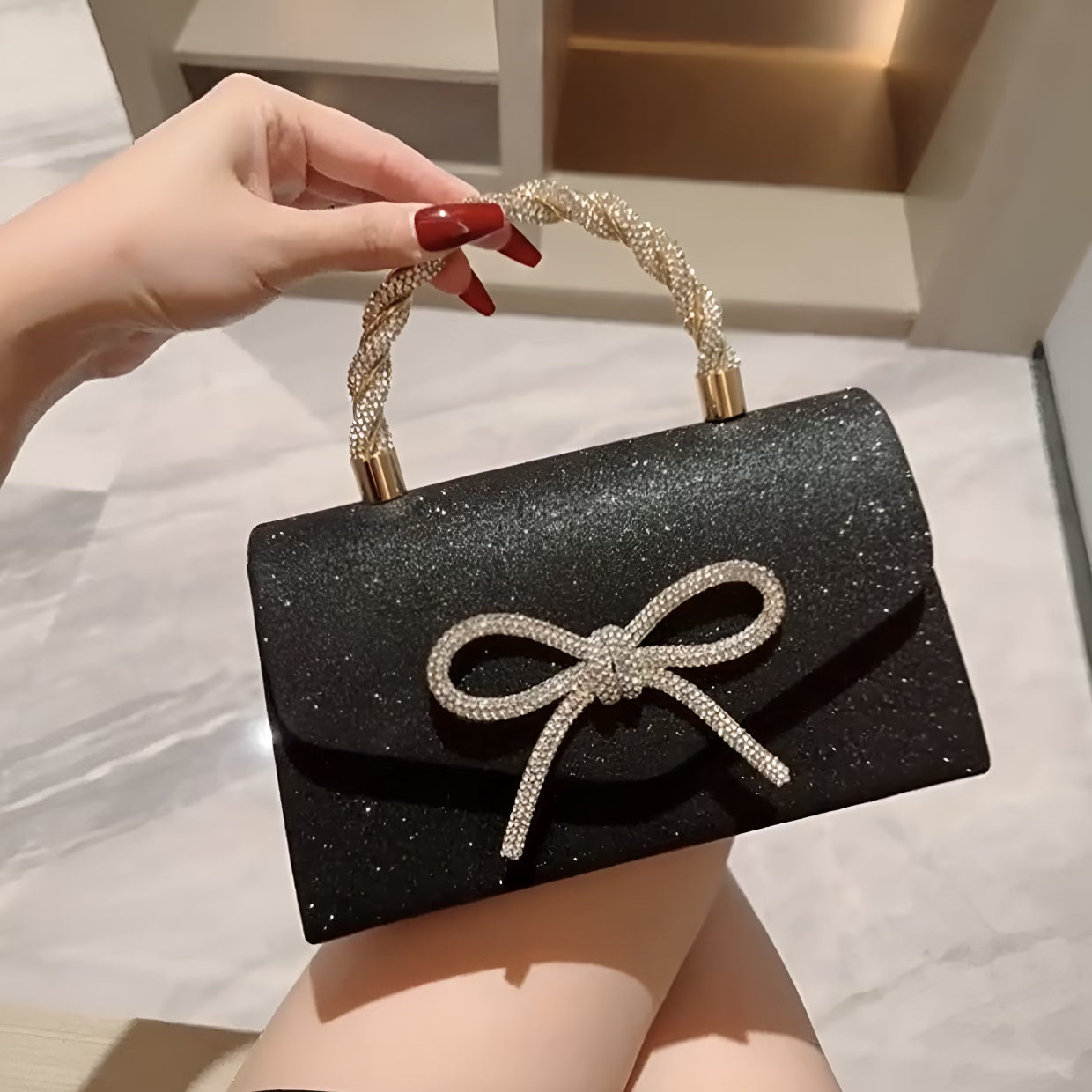 Black glittery handbag with a bow detail held by a hand.