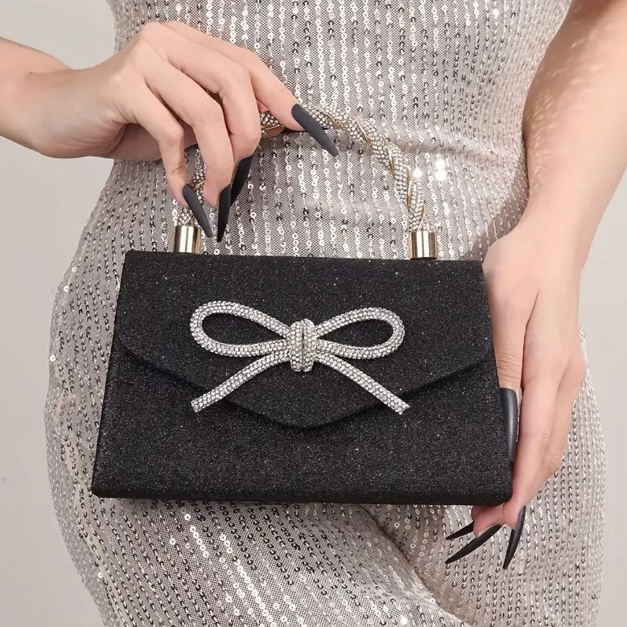Black clutch with a bow detail held by a person wearing a silver sequin dress.